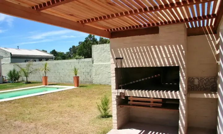 Parrillero bajo pérgola junto al jardín y la piscina